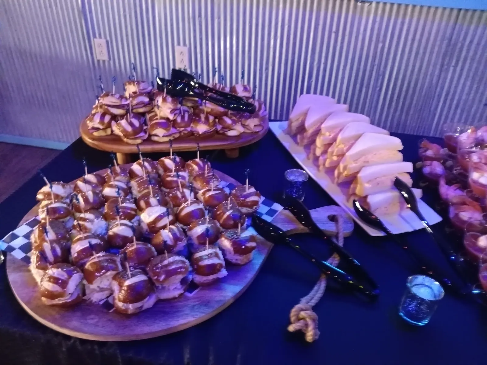Pretzel-bun sliders on wooden boards next to a platter of finger sandwiches