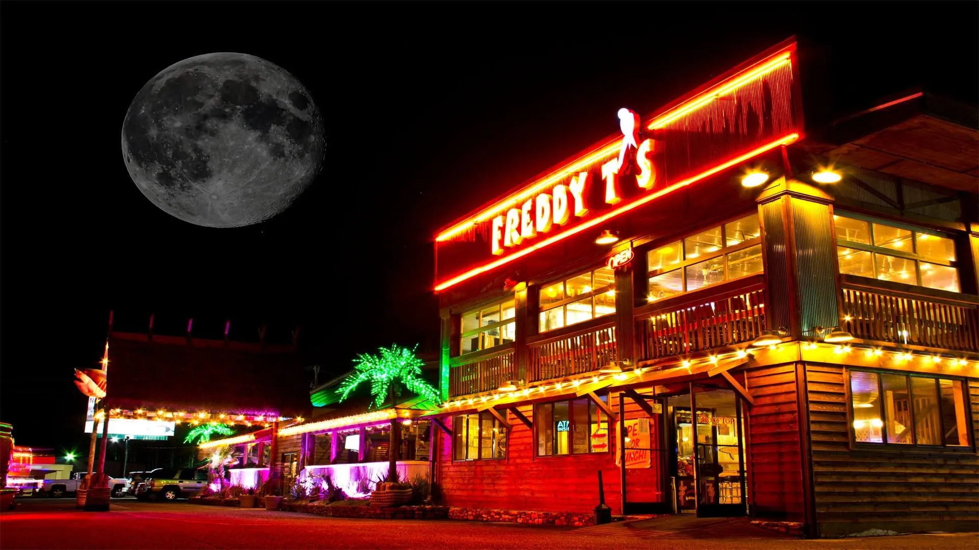 Freddy T's at night — red neon sign, lit windows and a neon palm tree on Highway 57